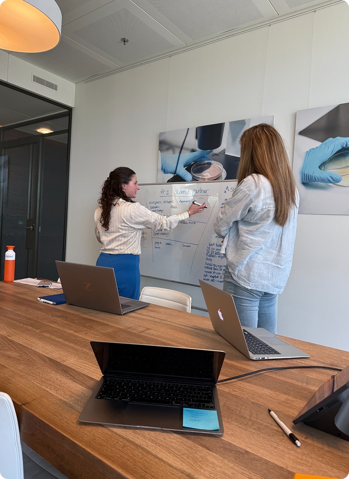 Brainstormsessie bij Kadans Science Partner waarbij Maureen en Valerie campagne-ideeën uitwerken op een whiteboard.