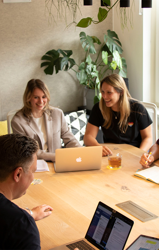 Karin van Solingen, Sandra Buitendijk en Mark Drenth zitten en lachen aan de werktafel van online marketingbureau Onest.